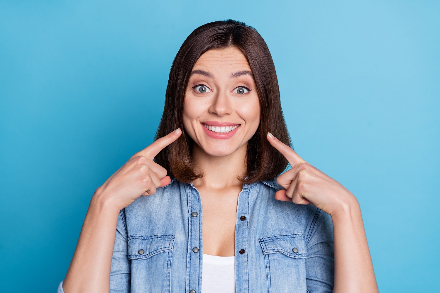 Person pointing to their bright, white teeth after treatment at Sunrise Dental Clinic in Gig Harbor, WA